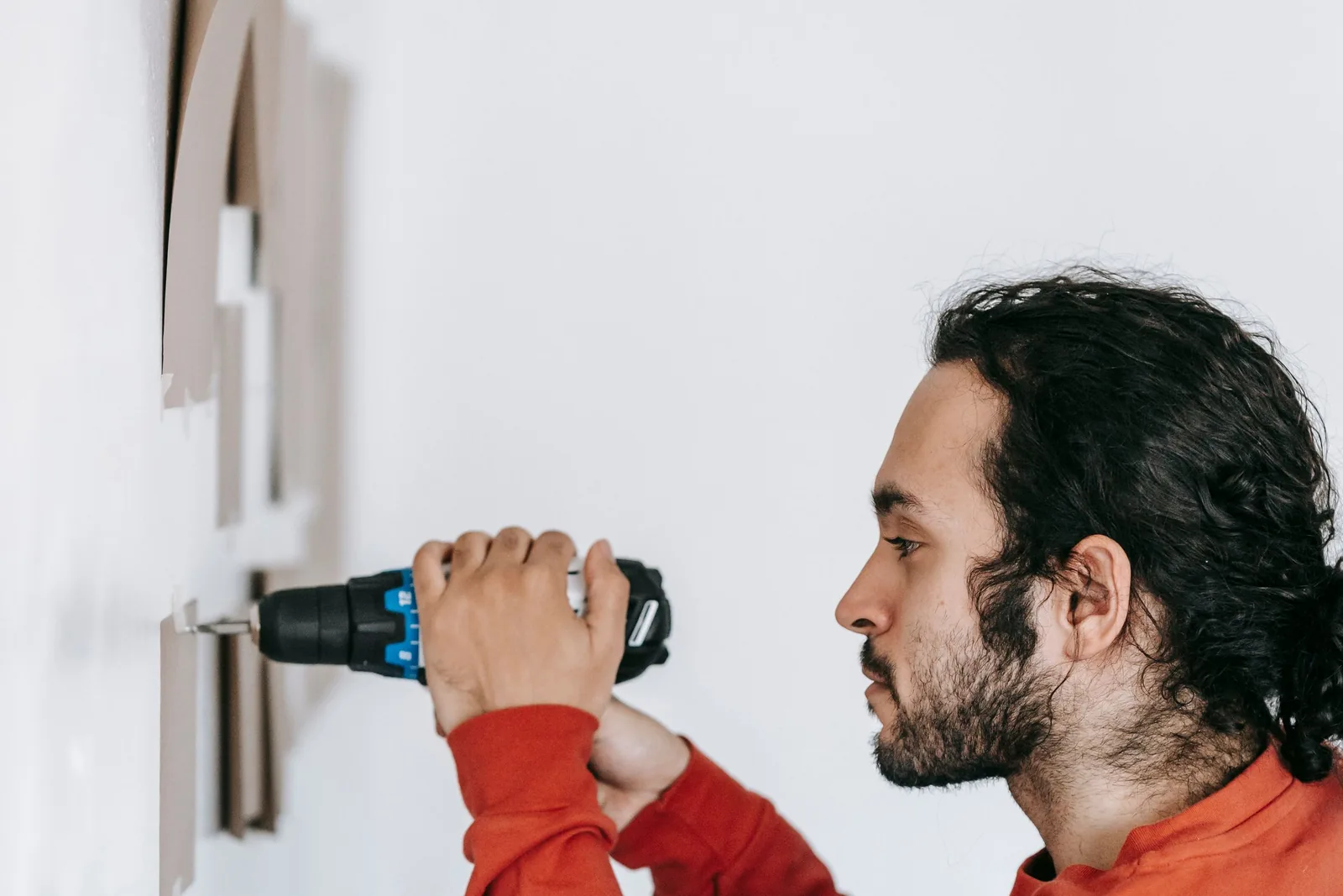 A contractor using a drill on an interior wall, accompanying this drywall repair and painting guide